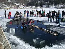  A diver is visible underwater in a hole cut in the ice cover of a small lake