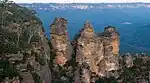 Rugged sandstone cliff face with three large pinnacles, surrounded by a forested valley