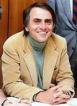 Color photo. Man sitting wearing a suit and smiling.