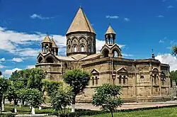 Stone church with a central tower topped by a conical roof and several smaller towers.