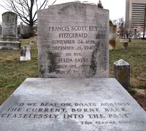 A color photograph of a grave. The headstone reads Francis Scott Key Fitzgerald September 24, 1896 December 21, 1940 His Wife Zelda Sayre July 24, 1900 March 10, 1948. "So we beat on boats against the current, borne back ceaselessly into the past" -- The Great Gatsby