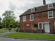 Photograph of a two-story brick house with dormer windows emerging from the roof to suggest a small third story.