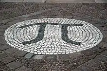 A photograph of the Greek letter pi, created as a large stone mosaic embedded in the ground.