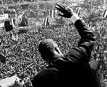 The back of a man waving to the throng below