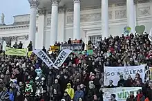 Many people standing on steps of large public building holding banners with signs, including "Act For Climate" and "Go Nuclear."