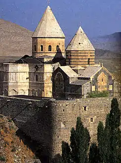 Stone church in the mountains with two massive towers topped by a conical roof