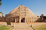 A large stupa in stone with an elaborate gate in front