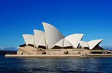 Beige and white building with seven peaked rooves, sitting on a promontory surrounded by water