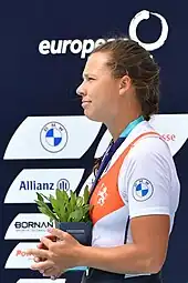 Bente Paulis schaut bei der Siegerehrung nach rechts. Sie trägt das niederländische Nationaltrikot über einem weißen T-Shirt. Um den Hals hängt ein blaues Band, an dem die nicht sichtbare Silbermedaille befestigt ist. In den Händen hält sie einen Blumentopf.