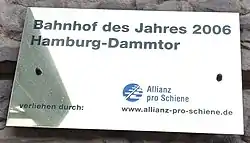 Etwa 20 mal 40 Zentimeter großes messingfarbenes Schild mit der Aufschrift „Bahnhof des Jahres 2006 Hamburg-Dammtor verliehen durch: Allianz pro Schiene“