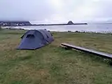 Foto eines Zeltes am Strand, im Hintergrund eine Insel und einige Häuser