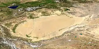 Satellitenaufnahme des Tarimbeckens mit der Taklamakan-Wüste; im Südwesten Ausläufer des Himalaya. Das Tian-Shan-Gebirge befindet sich im oberen Bildteil nördlich des Tarimbeckens. In der linken oberen Bildecke der Yssykköl-See. (NASA/MODIS/Blue Marble)