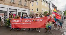 Das Foto zeigt Demonstrierende des CSD in Bayreuth, die ein Banner von SPD queer tragen. Geschrieben steht: „Stadt – Land – Bunt. Respekt für deine Vielfalt. SPD queer.“