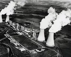 Kernkraftwerk Calder Hall an der Küste Cumbrias (1973). Die Kühltürme wurden 2007 abgerissen. Links direkt neben Calder Hall wurde die Wiederaufarbeitungsanlage THORP errichtet und betrieben. 3 von 4 Calder Hall Reaktorgebäuden stehen noch. Auf der restlichen Fläche (auf dem Bild unten) wurde die neue Silo Maintenance Facility errichtet, welche ab 2023 ihren Betrieb aufnehmen soll.