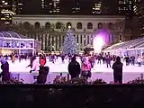 Eine Eisfläche im Park, mit geschmückten Weihnachtsbaum und Eisläufern.