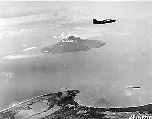 Hansa Bay im Luftbild einer B-24D Liberator der 5. Airforce aus 17.000 Fuß Höhe. Im Vordergrund steigt Rauch aus der Bombardierung von Awar Point (Condor Point) auf. In der Bucht liegt Laing Island, vor der Küste liegen die Stephan Strait und die Insel Manam. Februar 1944.