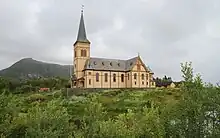 Foto einer Holzkirche, im Hintergrund eine Erhebung