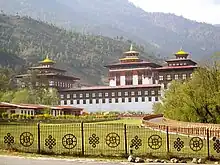 Tashichho Dzong, Verwaltungszentrum von Thimphu. Traditionelle Festung mit einem eingezäunten Park im Vordergrund. Der Eisenzaun des Parks ist mit glücksbringenden Symbolen verziert.