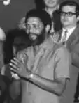 Maurice Bishop, New Jewel Movement. Schwarz-Weiß-Aufnahme eines bärtigen Afroamerikaners, der klatscht.