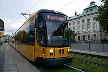 Eine Straßenbahn an einer Haltestelle vor einem Haus.