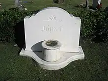 Grabstein von John ʻĪʻī auf dem Oahu Cemetery. Ein Grabstein aus weißem Marmor mit schlichter Schrift und einer einfachen, runden Vase davor.