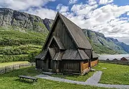 Foto einer hölzernen Stabkirche, im Hintergrund ein Bergmassiv und ein See