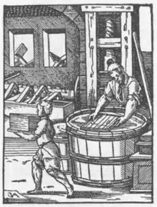 Papiermacher mit dem Schöpfsieb an der Bütte. Im Hintergrund die Gautschpresse, Jost Amman 1568