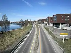 Foto einer Straße, die durch eine Stadt führt, links davon ein breiter Fluss