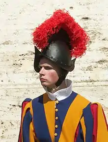 Farbige Nahaufnahme von einem Gardisten mit seinem schwarzen altertümlichen Helm aus Blech und mit rotem Federbusch.