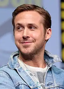 Ryan Gosling hat kurzes blondes Haar und einen Dreitagebart. Er trägt ein weißes Shirt und eine hellblaue Jeansjacke.