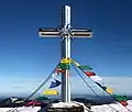 Gipfelkreuz mit Gebetsfahnen und Blick auf Sonnwendstein im Hintergrund