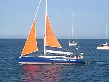 Das Bild zeigt ein Segelschiff mit zwei kleinen orangen Segeln