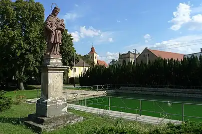 Dorfplatz von Vyšehořovice mit Statue des hl. Johannes von Nepomuk, Kirche St. Martin, Löschbassin und Ruine des Glockenturms