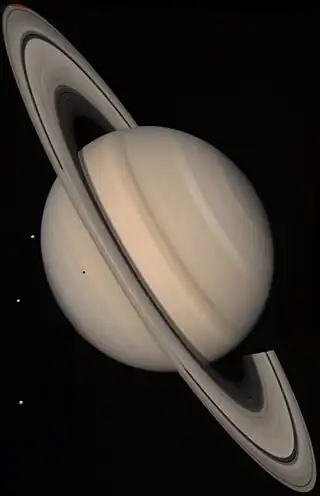 Saturno en veraj koloroj kun la lunoj Tetiso (kiu projekcias sian ombron), Diono kaj Reo.