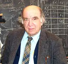 chest high portrait in suit and tie with longish hair in front of blackboard calculations